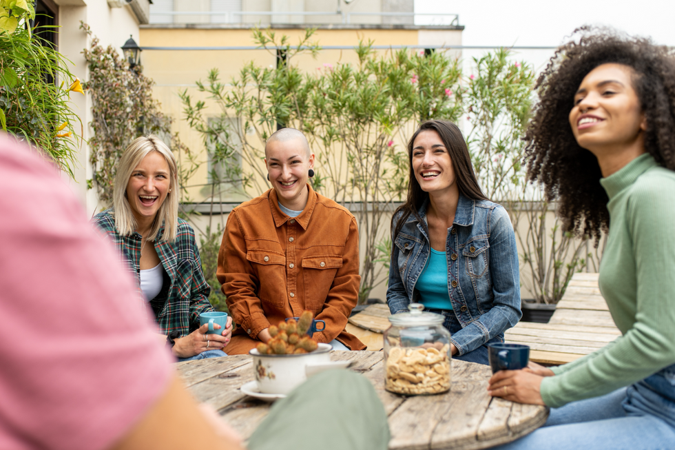 A group of women getting coffee together. They're outside at a rustic wooden table.