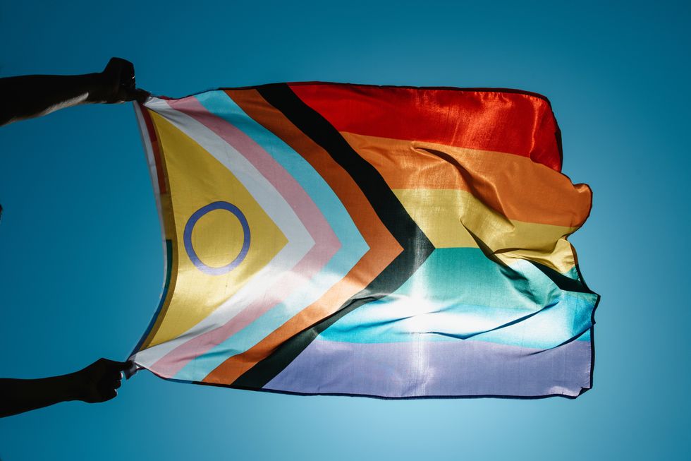 a man waves an intersex-inclusive progress pride flag in the wind on the sky