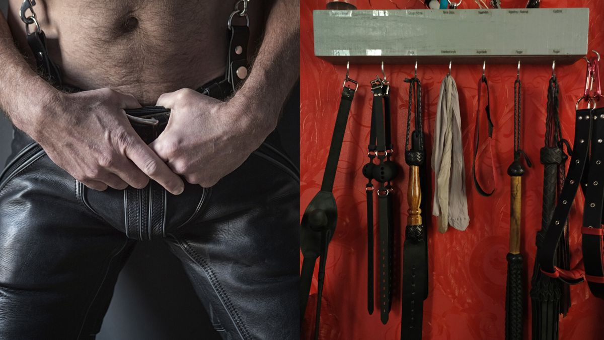 A wall of BDSM gear hung up on hooks against a red wall the toys include leather paddles floggers restraints and a ball gag.