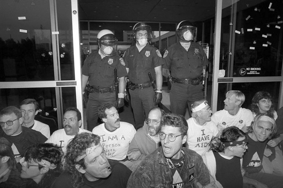 ACT UP activists sitting with their arms linked while police officers stand at their backs.