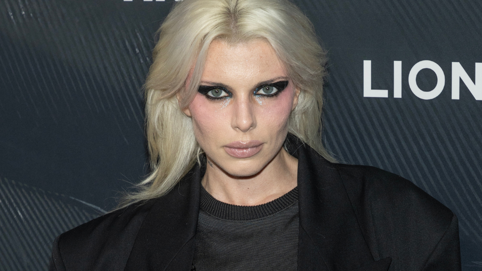 Actress and model Julia Fox on the red carpet. She is a 34-year-old Italian-American woman. She is thin, with platinum blonde hair that goes a few inches past her shoulders, a dramatic black eyeliner look, and a black blazer over a black top.