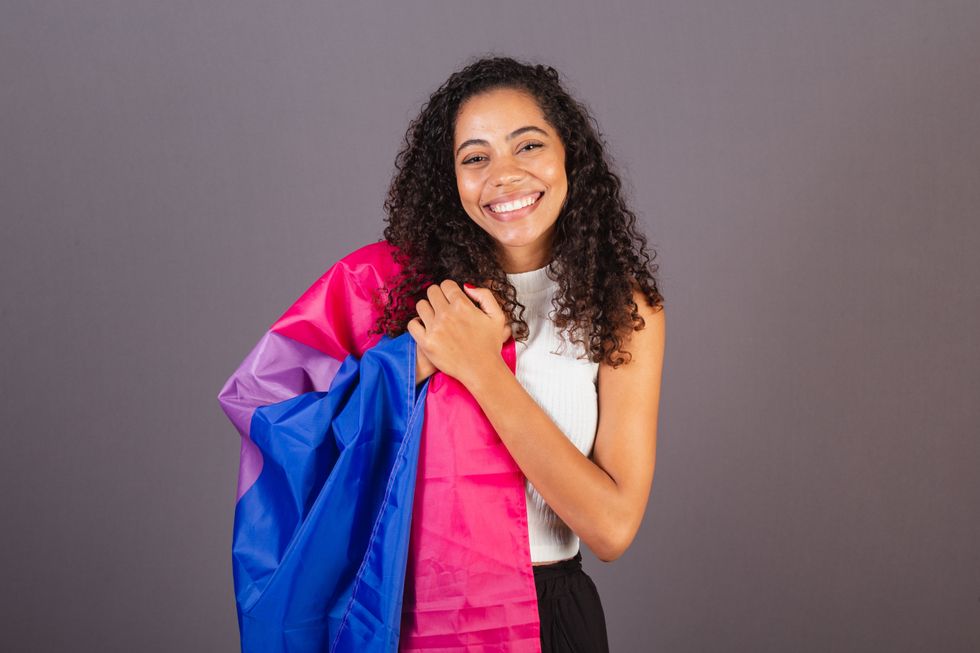 black woman holding a bisexual flag and smiling