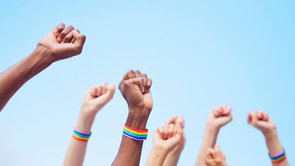 Cropped image of people raising arms with close fists wearing a lgbt bracelet