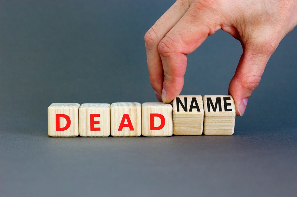 Deadname or name symbol. Concept words Deadname or Name on beautiful wooden blocks. Beautiful grey table grey background. Transgender hand. Business, deadname or name concept. Copy space.