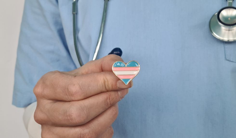 Doctor holding a heart shaped trans flag pin