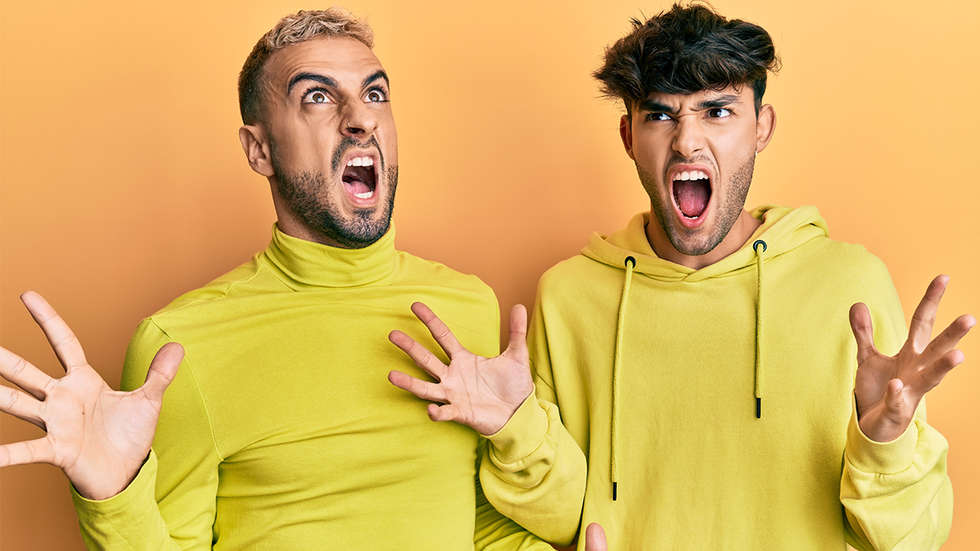 Homosexual gay couple standing together wearing yellow clothes crazy and mad shouting and yelling with aggressive expression and arms raised. frustration concept.