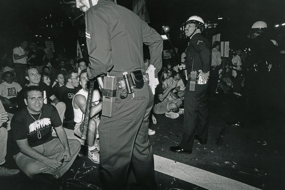 Polic eofficers standing in front of a group of ACT UP protesters who are sitting on the ground.