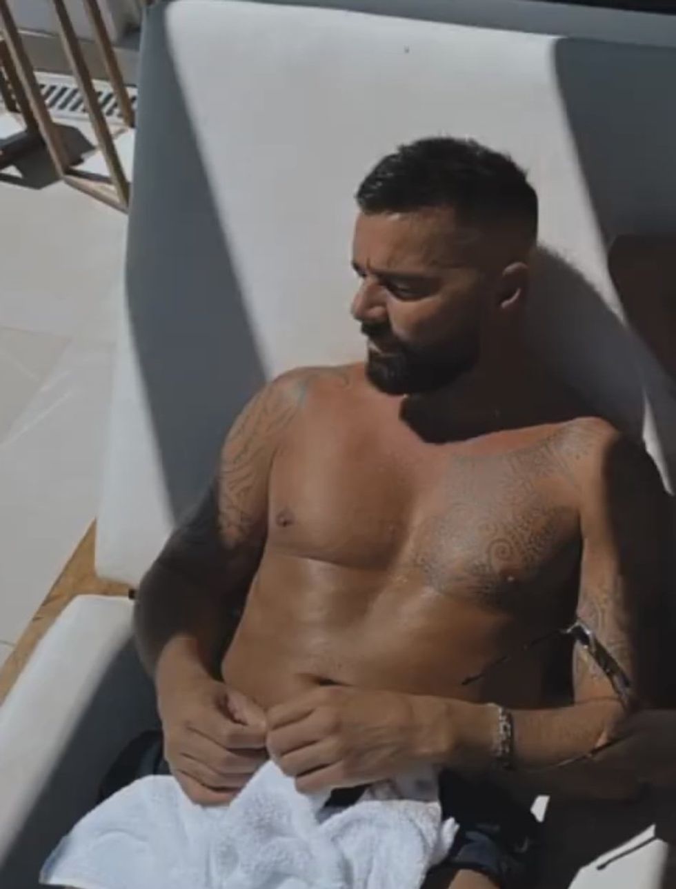 Ricky Martin, shirtless, sitting poolside.