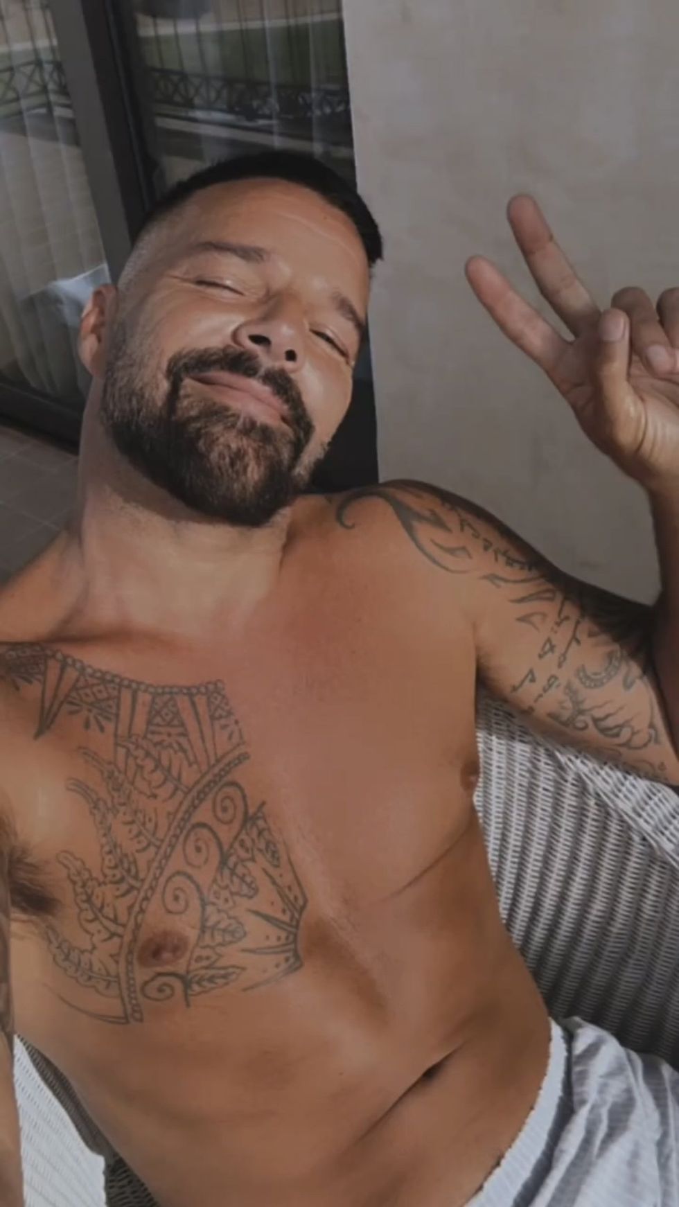 Ricky Martin, shirtless, taking a selfie and throwing up a peace sign.