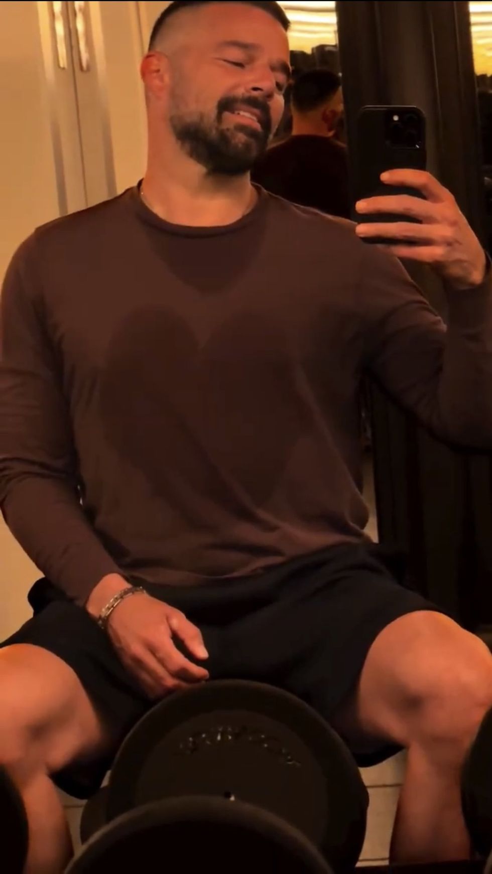 Ricky Martin taking a mirror selfie in a shirt soaked with sweat post workout.