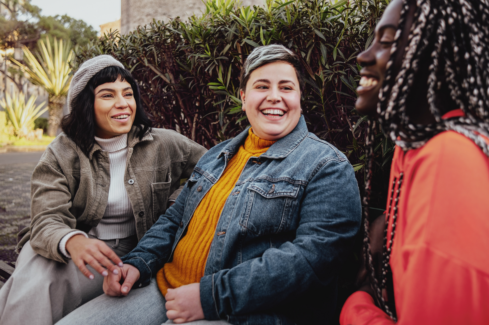 Three women sitting outside laughing. Two of the women are sitting closer together, looking warmly at the third.