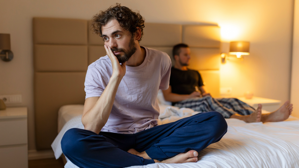 Two men sitting on opposite sides of a bed, not looking at one another.