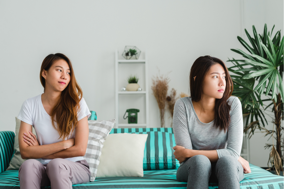 Two women sat on a couch. On the right, a woman is looking off into the distance at her left. On the left, woman is looking to the woman on the right.